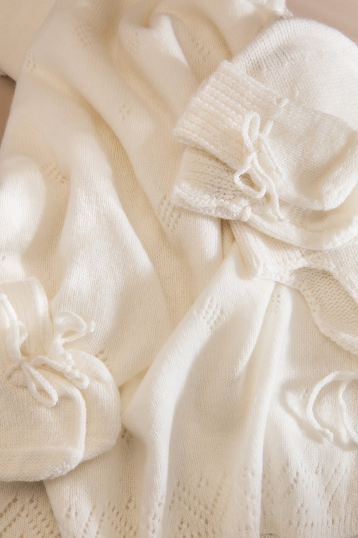 Johnstons of Elgin’s Gift Set includes our Cashmere Pointelle Baby Blanket, Hat, Mittens & Booties in Ecru on a beige background AW21GIFTSET18A