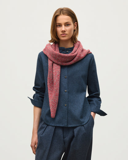 A model wearing a navy blue button-up shirt, matching navy trousers, and a textured pinkish-red scarf, photographed against a plain light gray studio background. JOHNSTONS OF ELGIN CASHMERE MARL KEILL TRIANGLE SCARF RED 100% CASHMERE HAB03648007014ONE