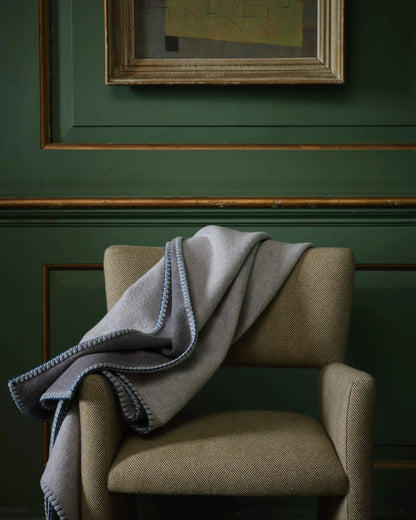 2025 Johnstons of Elgin Interiors Collection Silver & Grey Reversible Blanket Stitched Throw on an upholstered chair  TB000500RU7560ONE