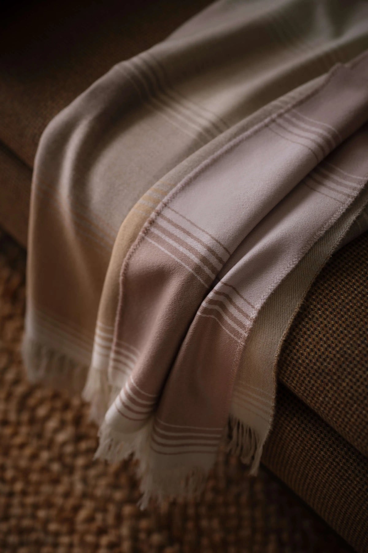 2025 Johnstons of Elgin Interiors Collection Camel & Pink Diffused Stripe Merino Wool Throw draped over the edge of a grey sofa WD000257RU7610ONE