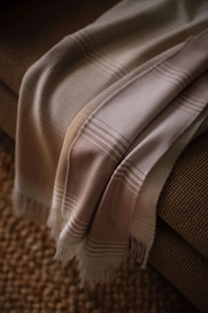 2025 Johnstons of Elgin Interiors Collection Camel & Pink Diffused Stripe Merino Wool Throw draped over the edge of a grey sofa WD000257RU7610ONE