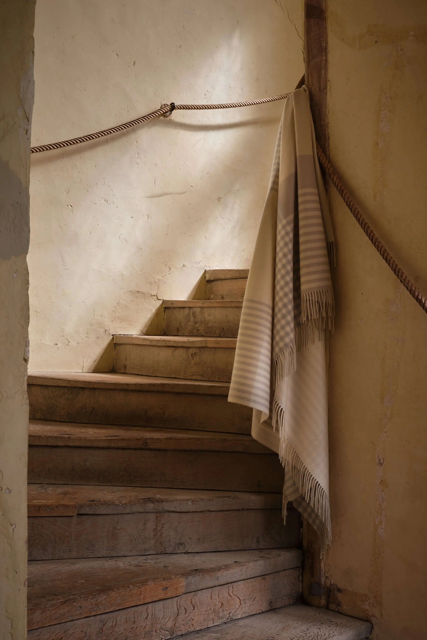 A luxurious cashmere throw draped elegantly on a stairway, showcasing the Heron Check design from the Johnstons of Elgin 2025 collection WA000013RU7604ONE
