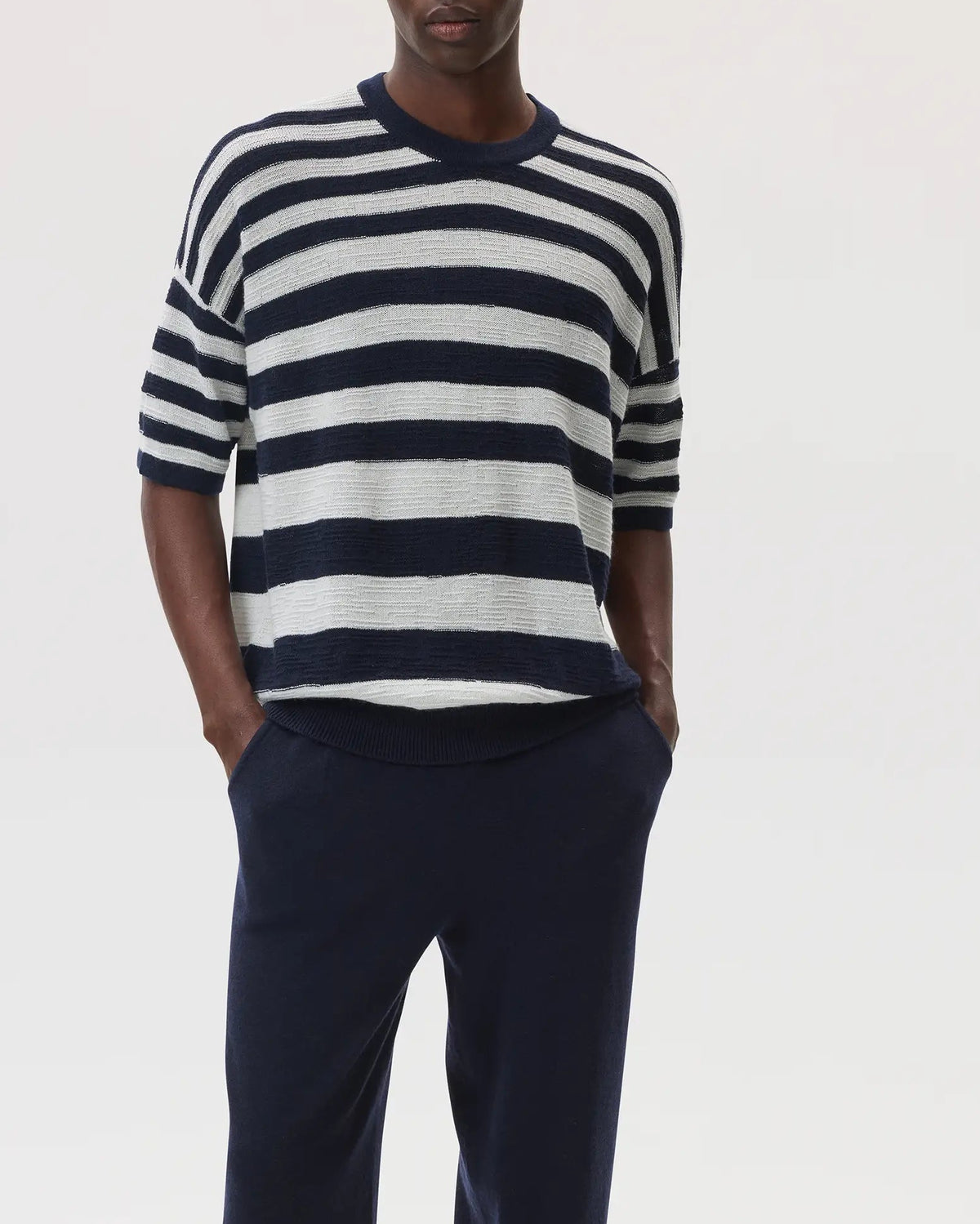 Male model wearing Johnstons of Elgin SS25 Unisex Knitwear Navy & White Textured Stripe Oversized Cashmere T-Shirt with navy cashmere joggers KAA05414Q25123