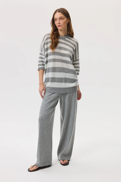 Female model wearing Johnstons of Elgin SS25 Unisex Knitwear Light Grey & White Textured Stripe Oversized Cashmere T-Shirt with grey wide leg trousers on a white backdrop KAA05414Q25124