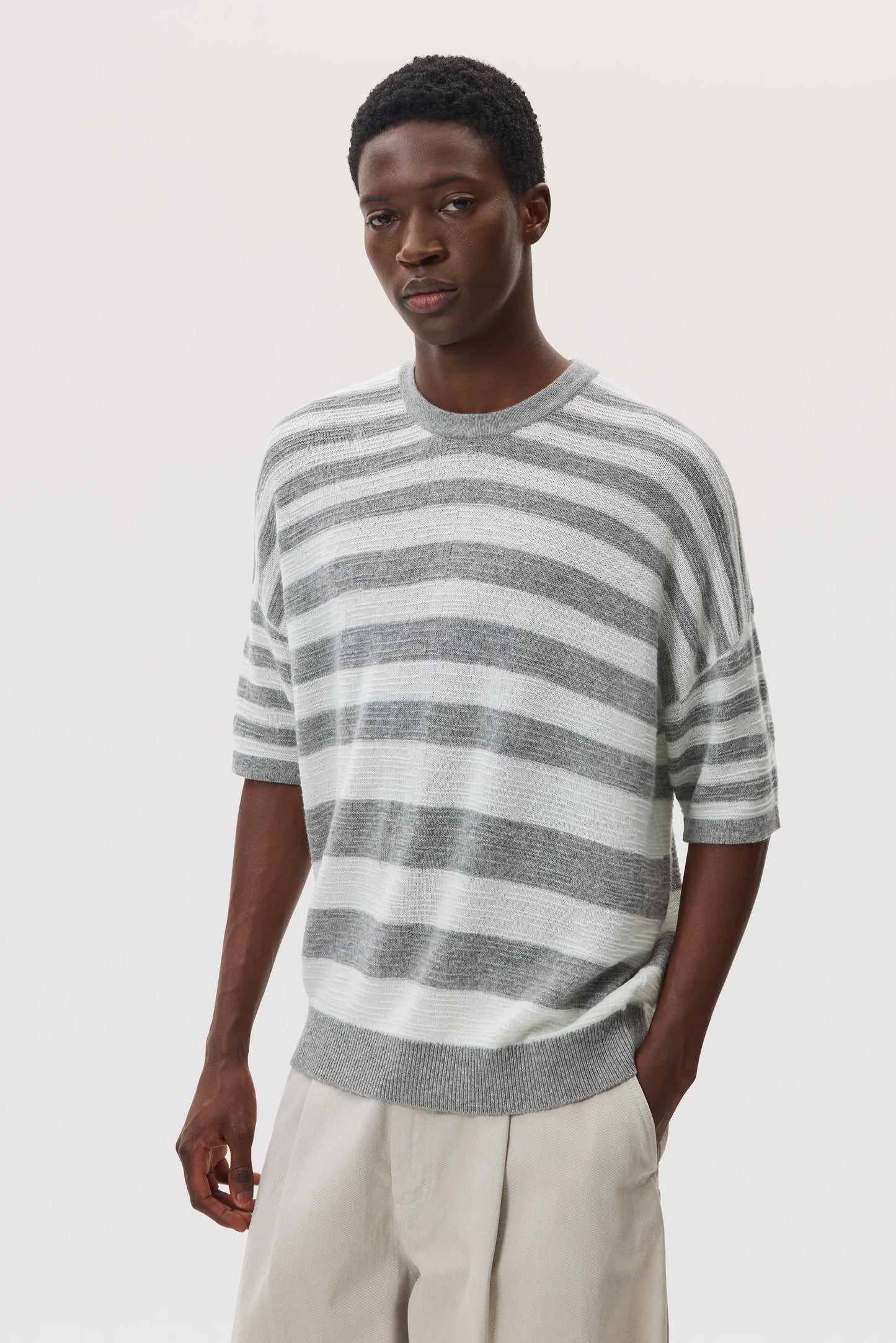 Male model wearing Johnstons of Elgin SS25 Unisex Knitwear Light Grey & White Textured Stripe Oversized Cashmere T-Shirt on a white backdrop KAA05414Q25124