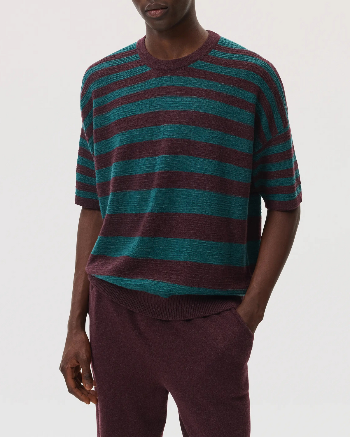 Male model wearing Johnstons of Elgin SS25 Unisex Knitwear Rosewood & Emerald Striped Oversized Cashmere T-Shirt with rosewood cashmere joggers KAA05414Q25125