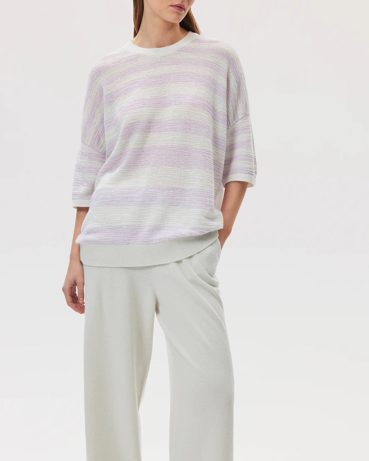 Female model wearing Johnstons of Elgin SS25 Unisex Knitwear White & Lavender Textured Stripe Oversized Cashmere T-Shirt with white wide leg trousers on a white background KAA05414Q25126