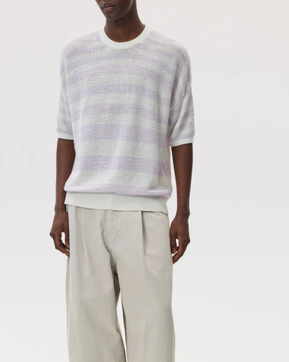 Male model wearing Johnstons of Elgin SS25 Unisex Knitwear White & Lavender Textured Stripe Oversized Cashmere T-Shirt with cream trousers and black sandals on a white background KAA05414Q25126