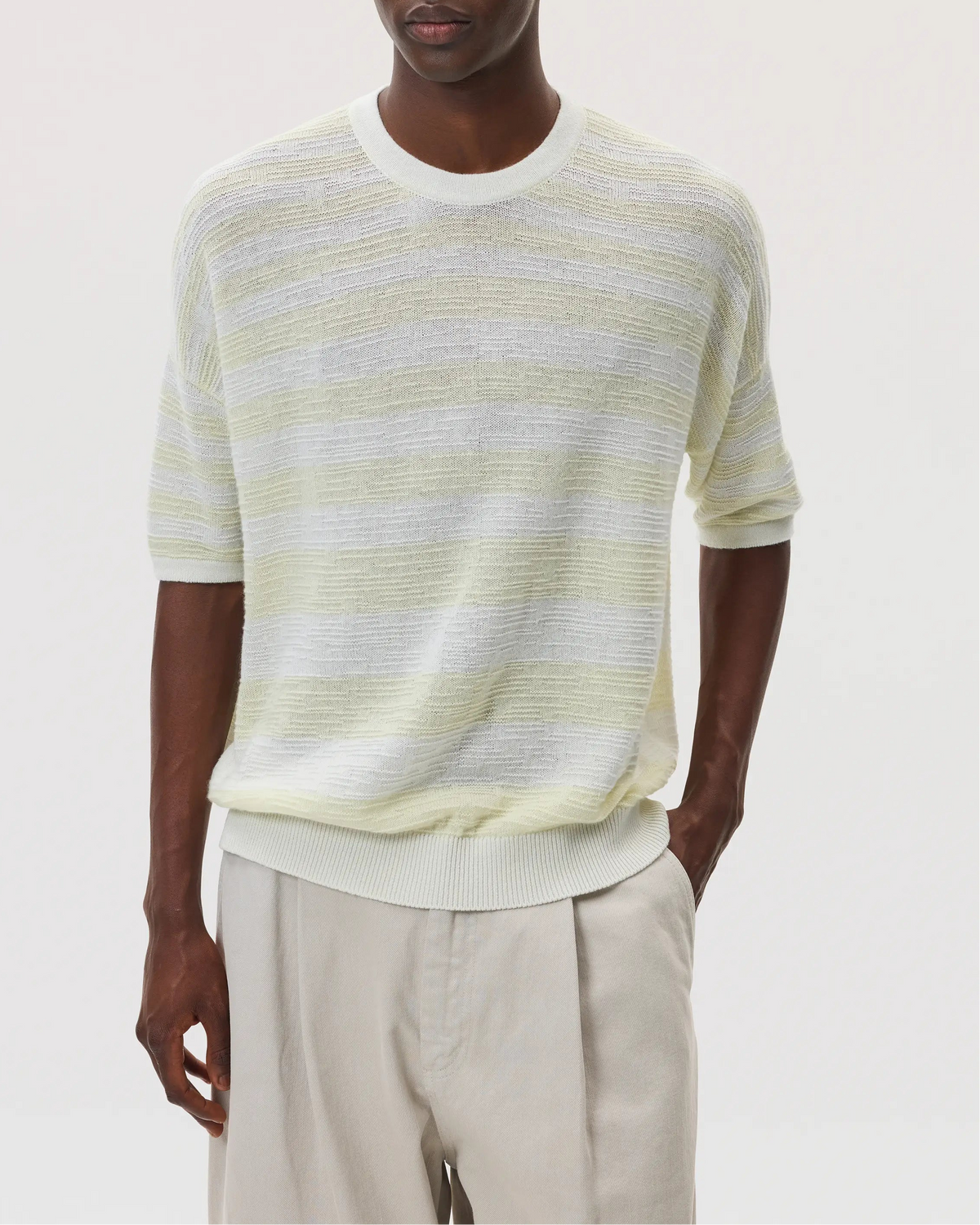 Male model wearing Johnstons of Elgin SS25 Unisex Knitwear White & Lemon Textured Stripe Oversized Cashmere T-Shirt with cream chino trousers against a white backdrop  KAA05414Q25127