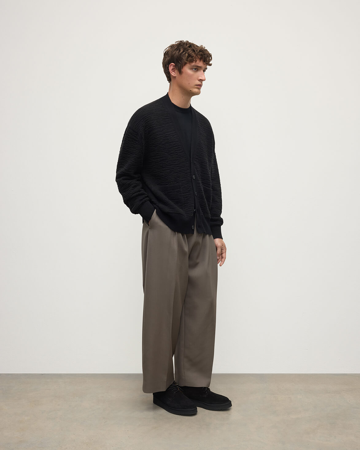 Model wearing Johnstons of Elgin AW25 Men's Knitwear Black & Iron Plaited Texture Black Cashmere Cardigan Side View KAA05579Q25387