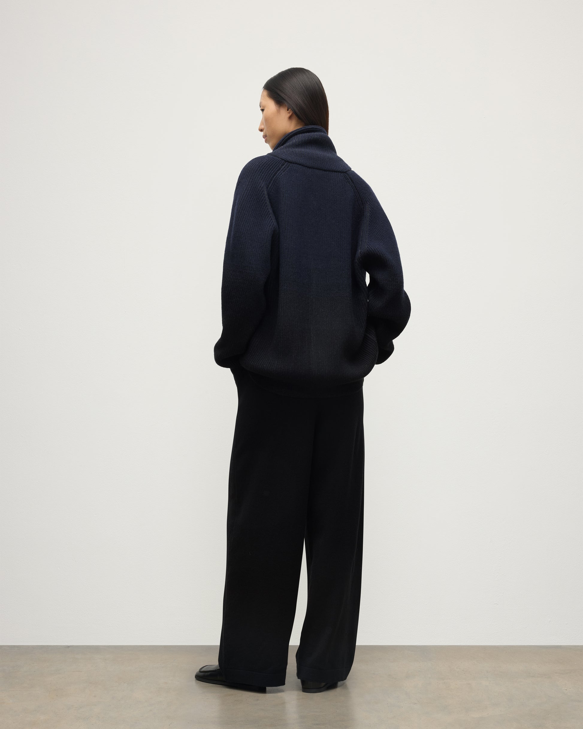 BACK OF FEMALE MODEL WEARING JOHNSTONS OF ELGIN PIONEER SHAWL CARDIGAN NAVY & BLACK 100% CASHMERE WITH BLACK TROUSERS AND POLO SHIRT UAA05750Q25947