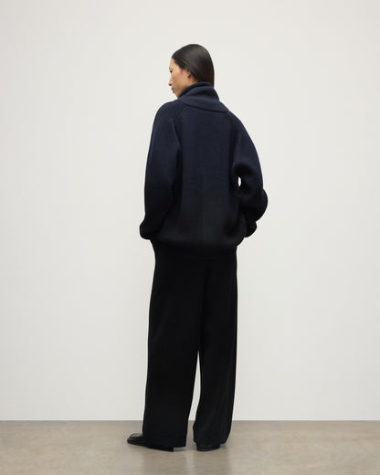 BACK OF FEMALE MODEL WEARING JOHNSTONS OF ELGIN PIONEER SHAWL CARDIGAN NAVY & BLACK 100% CASHMERE WITH BLACK TROUSERS AND POLO SHIRT UAA05750Q25947