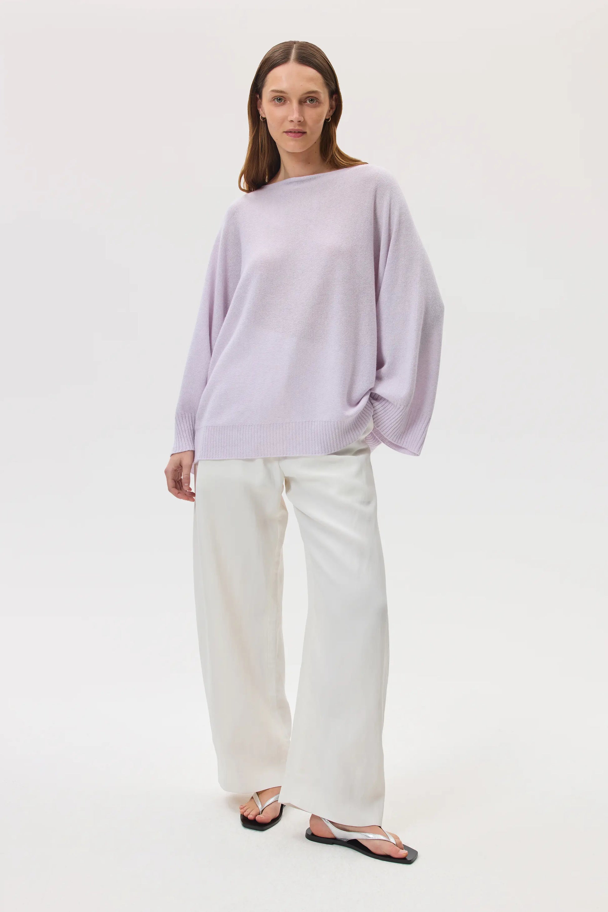 Model wears Johnstons of Elgin SS25 Women's Knitwear Lavender Cashmere Cape Jumper with white trousers KAI05048HD0086