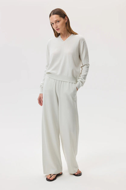 Model wearing Johnstons of Elgin SS25 Women's Knitwear White Classic Cashmere V Neck with white cashmere culottes on a white background  KAI05143HA0346