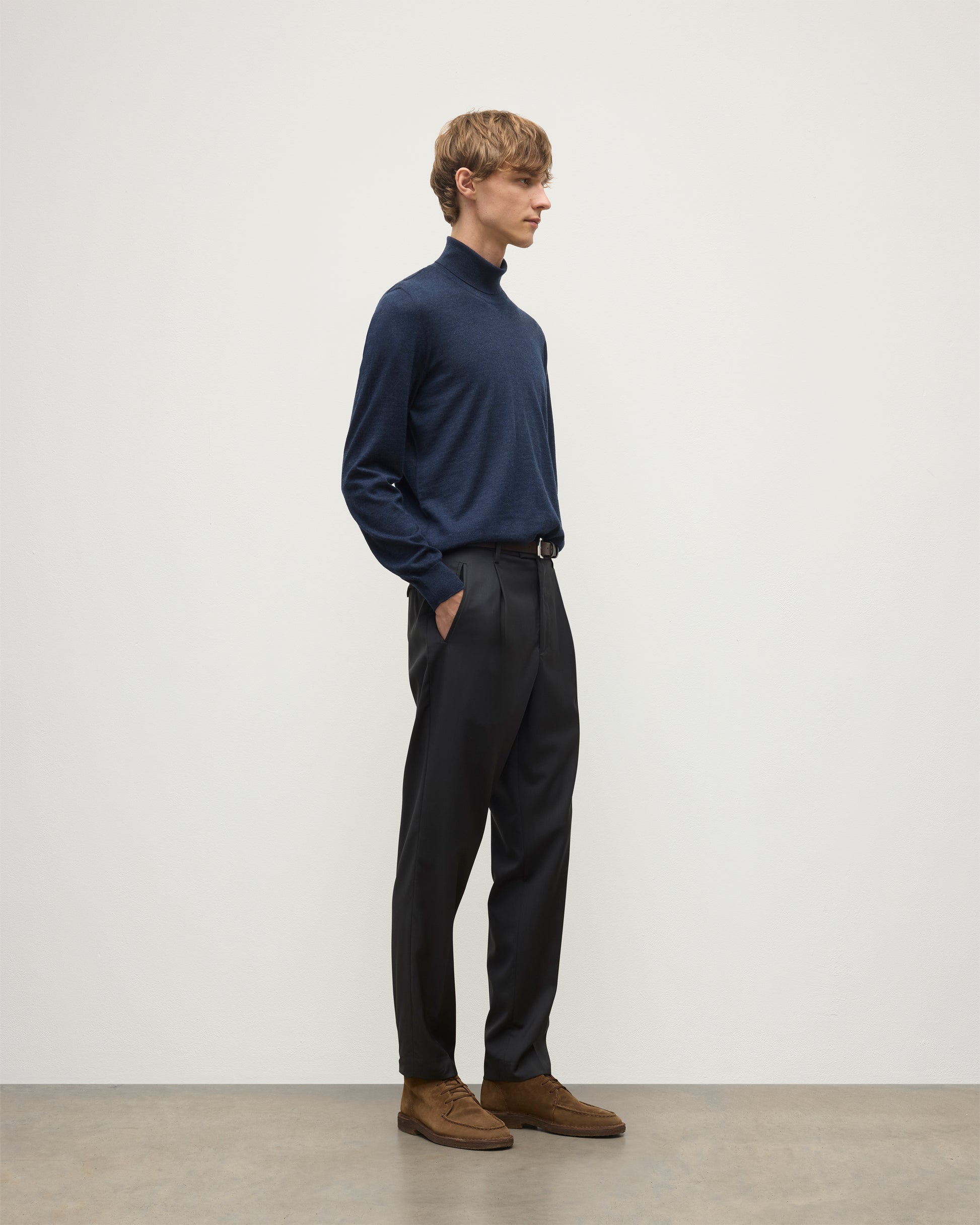 MODEL WEARS JOHNSTONS OF ELGIN MENS SUPERFINE FIN ROLL COLLAR NAVY 100% SUPERFINE CASHMERE  WITH GREY TROUSERS AND BROWN BELT KAI05333HD7350