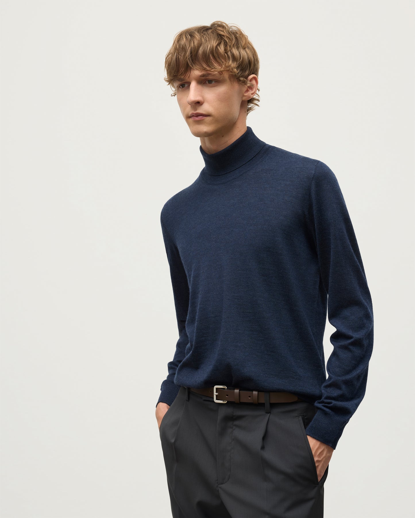 MODEL WEARS JOHNSTONS OF ELGIN MENS SUPERFINE FIN ROLL COLLAR NAVY 100% SUPERFINE CASHMERE  WITH GREY TROUSERS AND BROWN BELT KAI05333HD7350