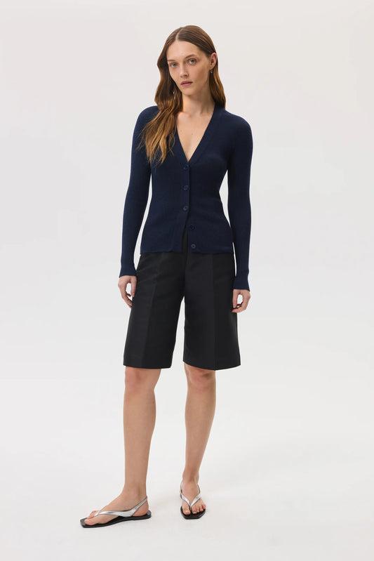 Model wearing Johnstons of Elgin SS25 Women's Knitwear Navy Superfine Cashmere Ribbed Cardigan with black shorts on a white backdrop KAI05372SD7600