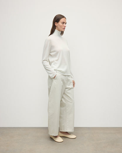 Model wearing Johnstons of Elgin AW25 Women's Knitwear Zinc White Superfine Cashmere White Roll Neck Jumper Side View  KAI05607HA0327