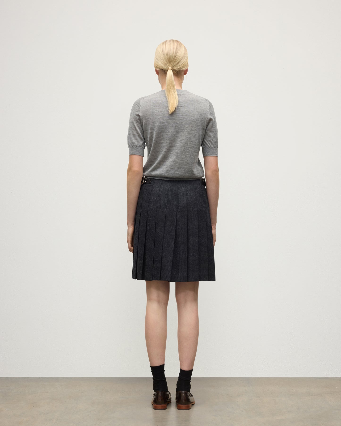 BACK VIEW OF A MODEL WEARING JOHNSTONS OF ELGIN WOMENS HONOR SHORT SLEEVE CREW GREY 100% SUPERFINE CASHMERE WITH SHORT LE KILT CHARCOAL KILT  KAI05712HA4253