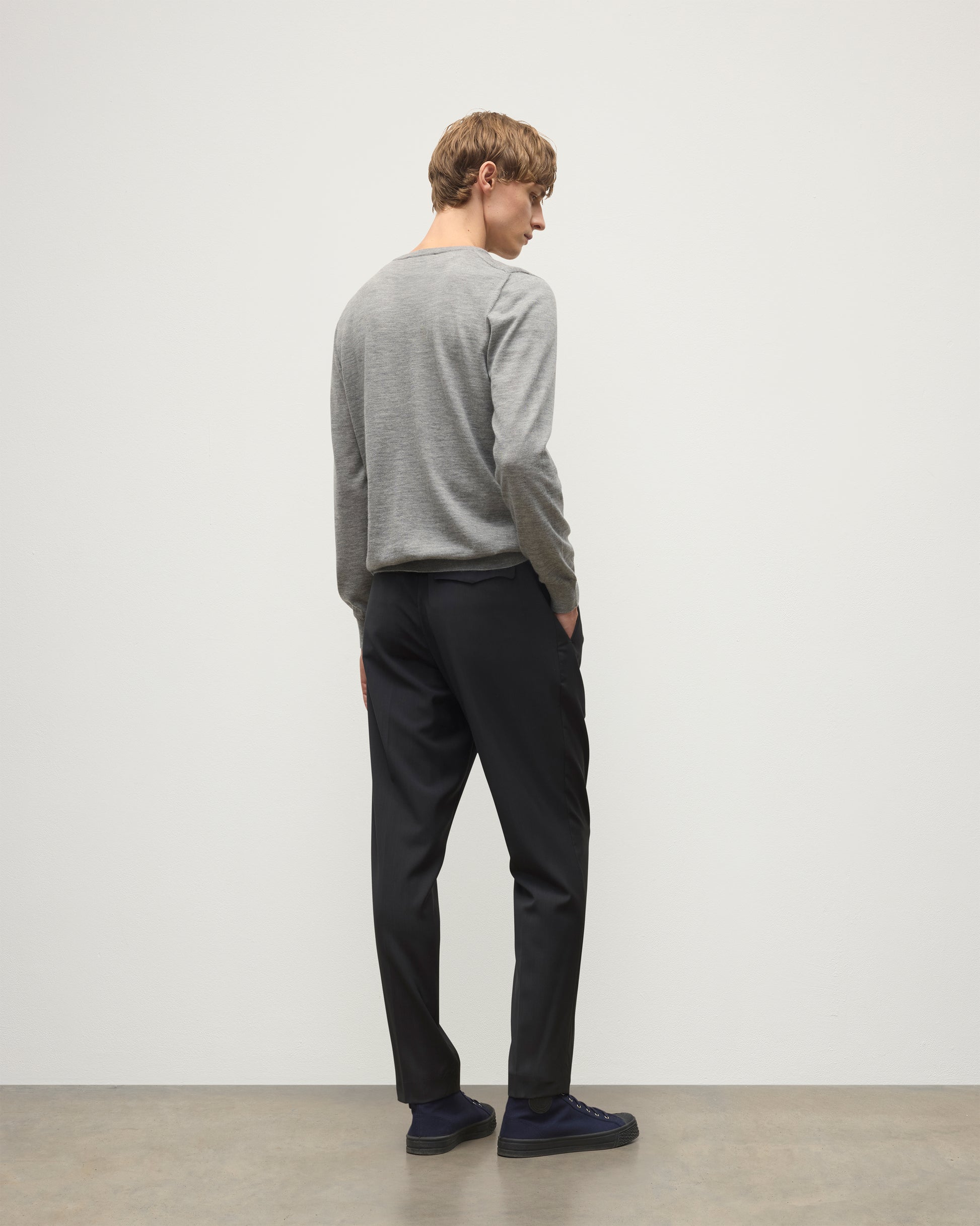 MODEL WEARS JOHNSTONS OF ELGIN MENS FIN SUPERFINE CREW GREY 100% SUPERFINE CASHMERE  OVER A WHITE T-SHIRT WITH GREY TROUSERS KAI05717HA4253