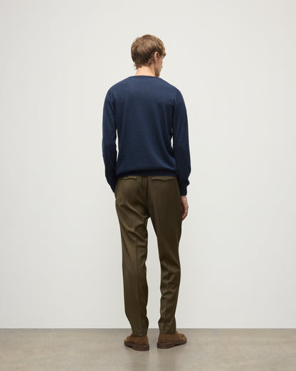 MODEL WEARING JOHNSTONS OF ELGIN MENS FIN SUPERFINE CREW NAVY 100% SUPERFINE CASHMERE OVER A WHITE T-SHIRT WITH OLIVE TROUSERS KAI05717HD7350