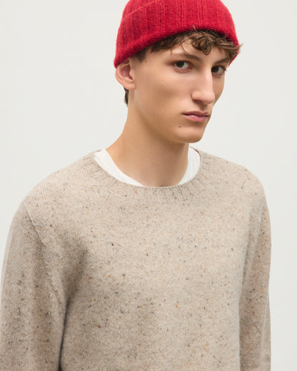 A man wearing a red knit beanie and a light beige speckled crewneck sweater over a white undershirt, photographed against a plain light gray background. JOHNSTONS OF ELGIN TIREE CREW SWEATER DONEGAL CASHMERE CREW SWEATER CREAM 100% CASHMERE KAI05755HA0397
