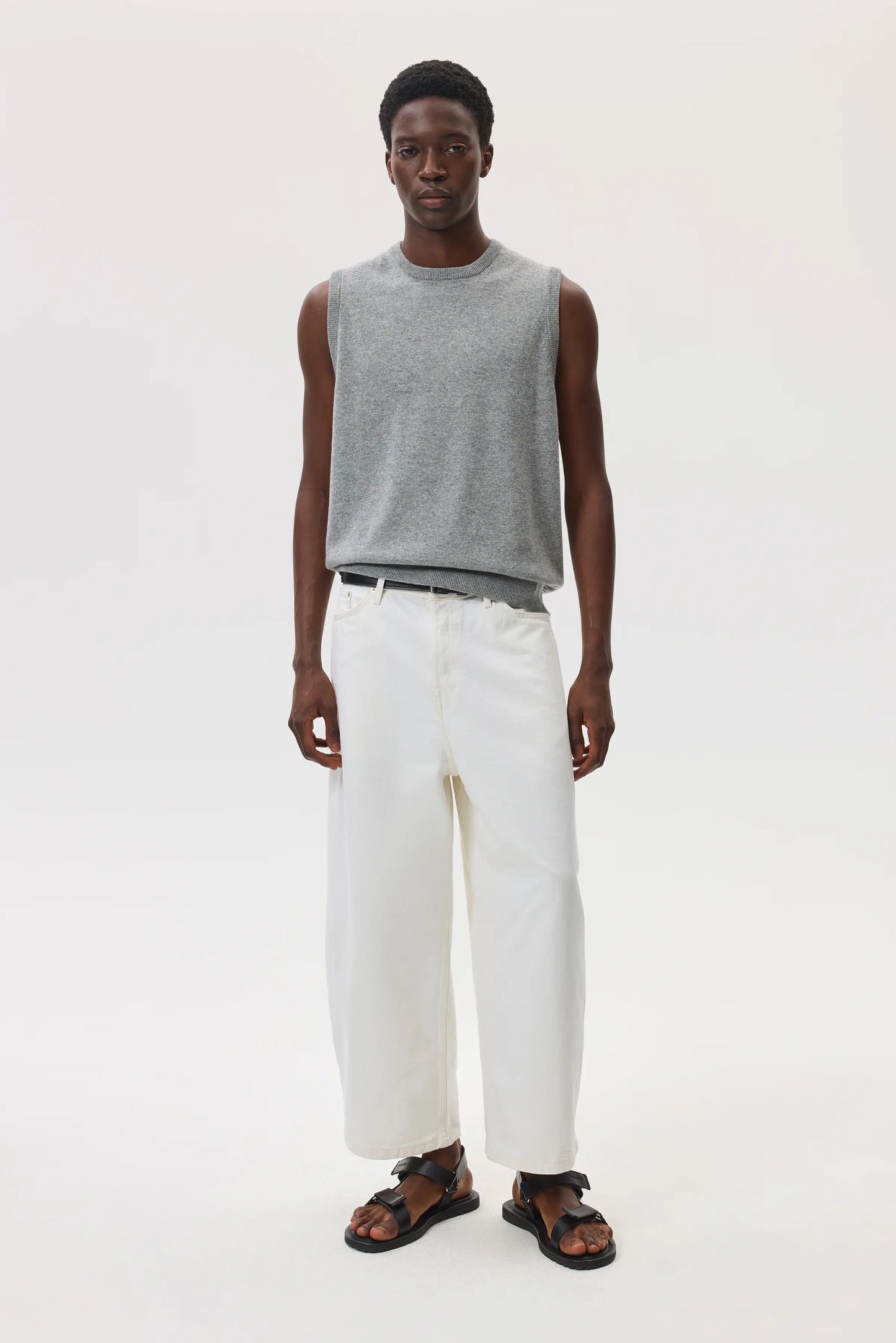 Male model wearing Johnstons of Elgin SS25 Unisex Knitwear Light Grey Cashmere Tank and white trousers against a white background  KAP05243HA0308