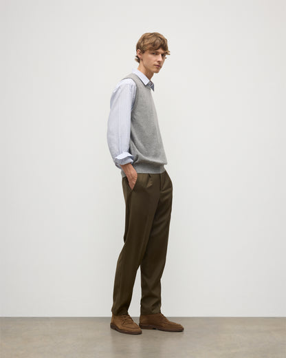 MODEL WEARS JOHNSTONS OF ELGIN MENS LENNOX SLEEVELESS CREW GREY 100% CASHMERE OVER A LIGHT BLUE SHIRT WITH OLIVE GREEN TROUSERS KAP05243HA0400