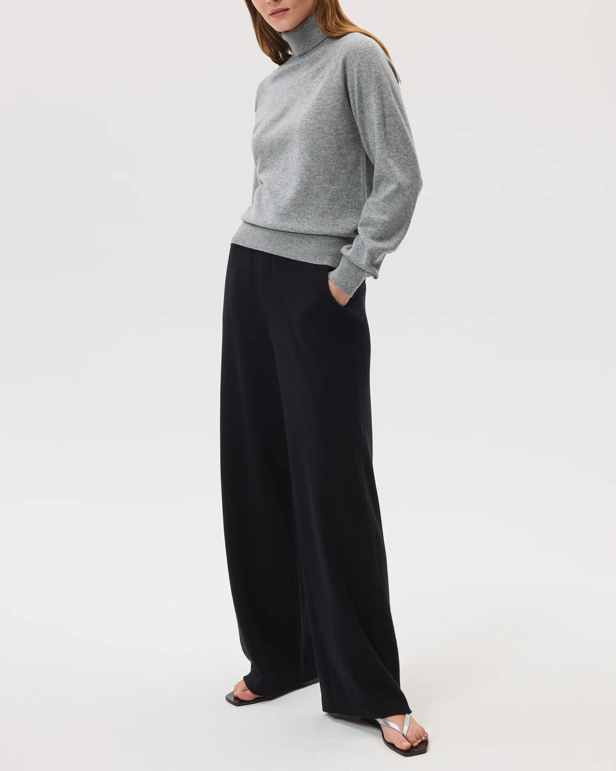 Model wears Johnstons of Elgin SS25 Women's Knitwear Light Grey Classic Cashmere Roll Neck Sweater with black wide leg trousers on a white background KAP05275HA0308