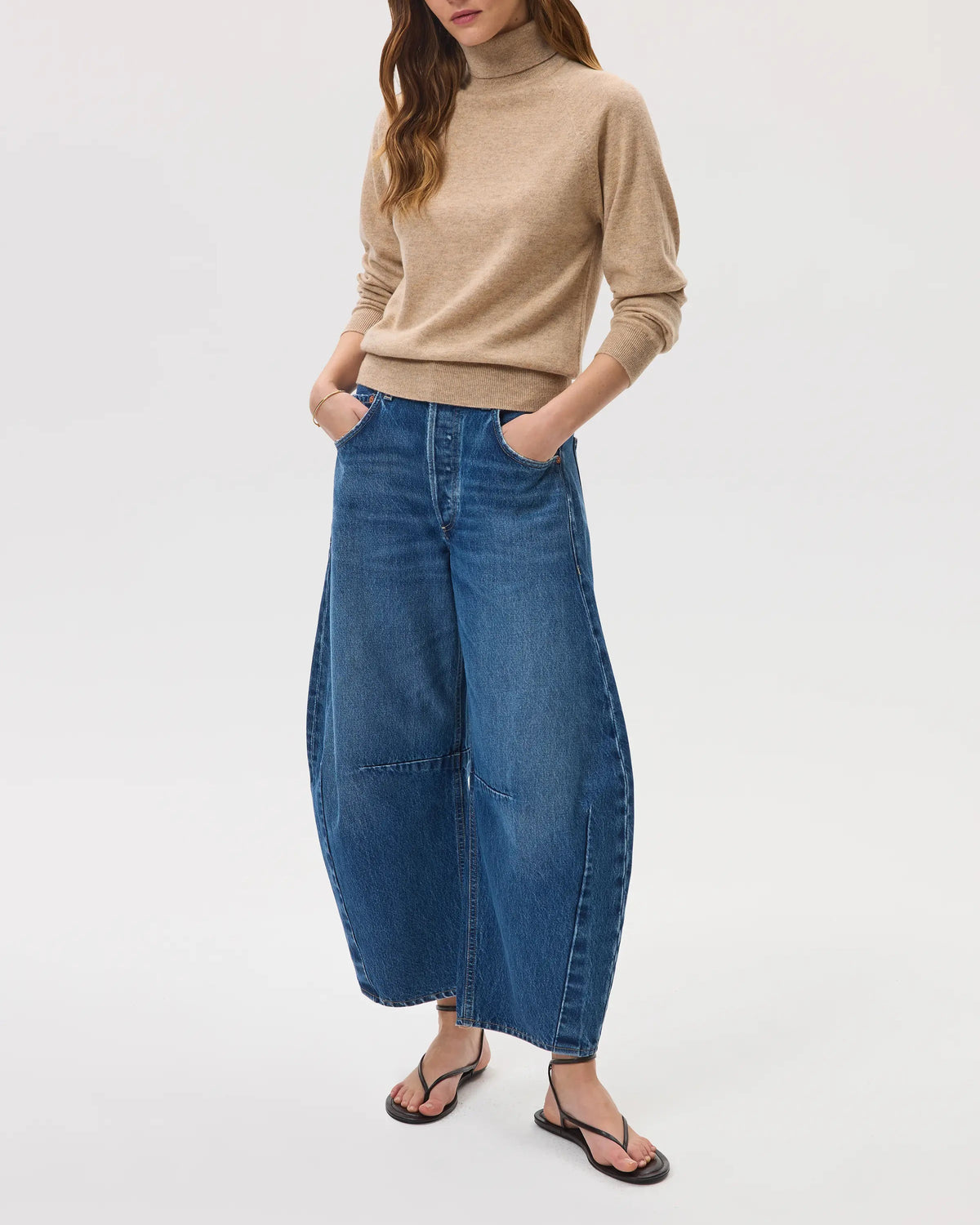 Model wears Johnstons of Elgin SS25 Women's Knitwear Oatmeal Classic Cashmere Roll Neck Jumper with blue jeans on a white background KAP05275HB0210