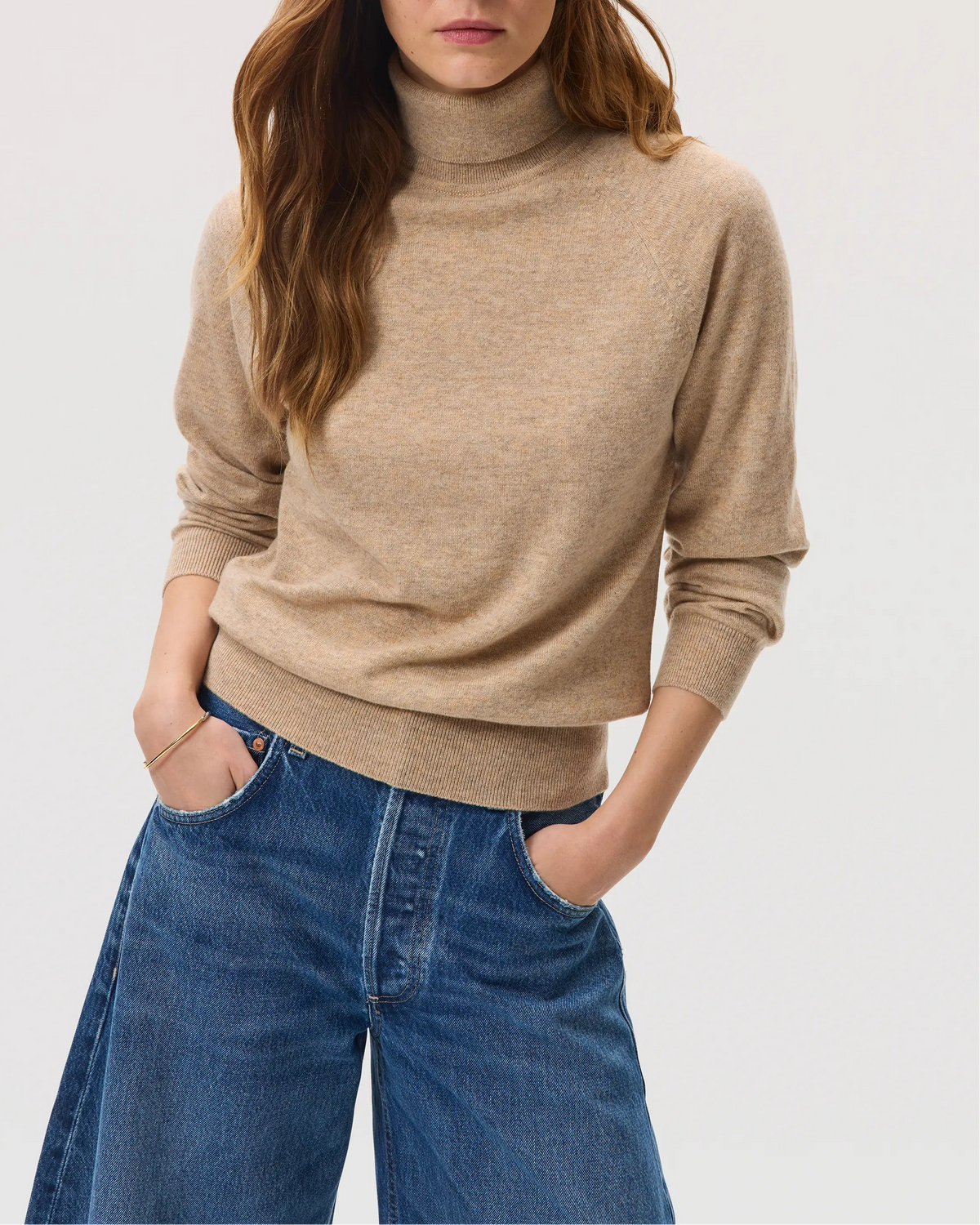 Model wears Johnstons of Elgin SS25 Women's Knitwear Oatmeal Classic Cashmere Roll Neck Jumper with blue jeans KAP05275HB0210