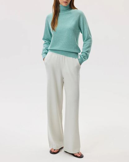 Model wears Johnstons of Elgin SS25 Women's Knitwear Jade Classic Cashmere Roll Neck Sweater with white culottes on white background KAP05275HC4284