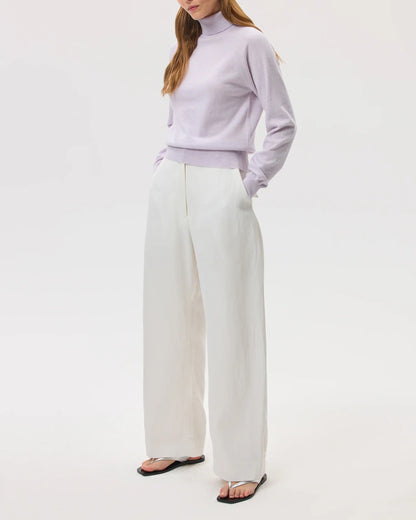 Model wears Johnstons of Elgin SS25 Women's Knitwear Lavender Classic Cashmere Roll Neck Jumper with white trousers on a white backdrop KAP05275HD0086