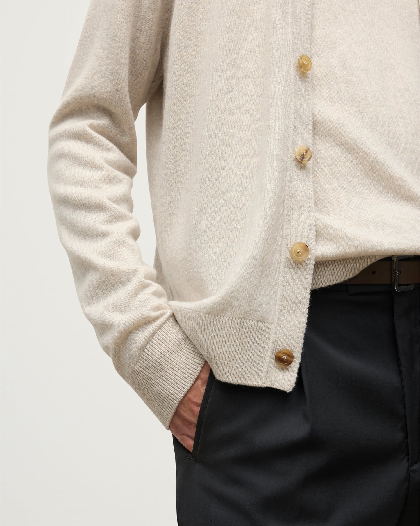 MODEL WEARS JOHNSTONS OF ELGIN MENS RORY VEE NECK CLASSIC CARDIGAN NATURAL 100% CASHMERE OVER A MATCHING V NECK SWEATER WITH GREY TROIUSERS KAP05576HA0402