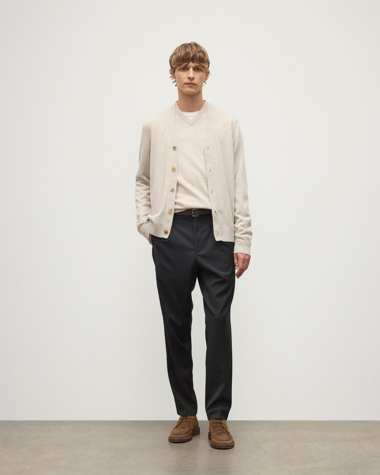 MODEL WEARS JOHNSTONS OF ELGIN MENS RORY VEE NECK CLASSIC CARDIGAN NATURAL 100% CASHMERE OVER A MATCHING V NECK SWEATER WITH GREY TROIUSERS KAP05576HA0402