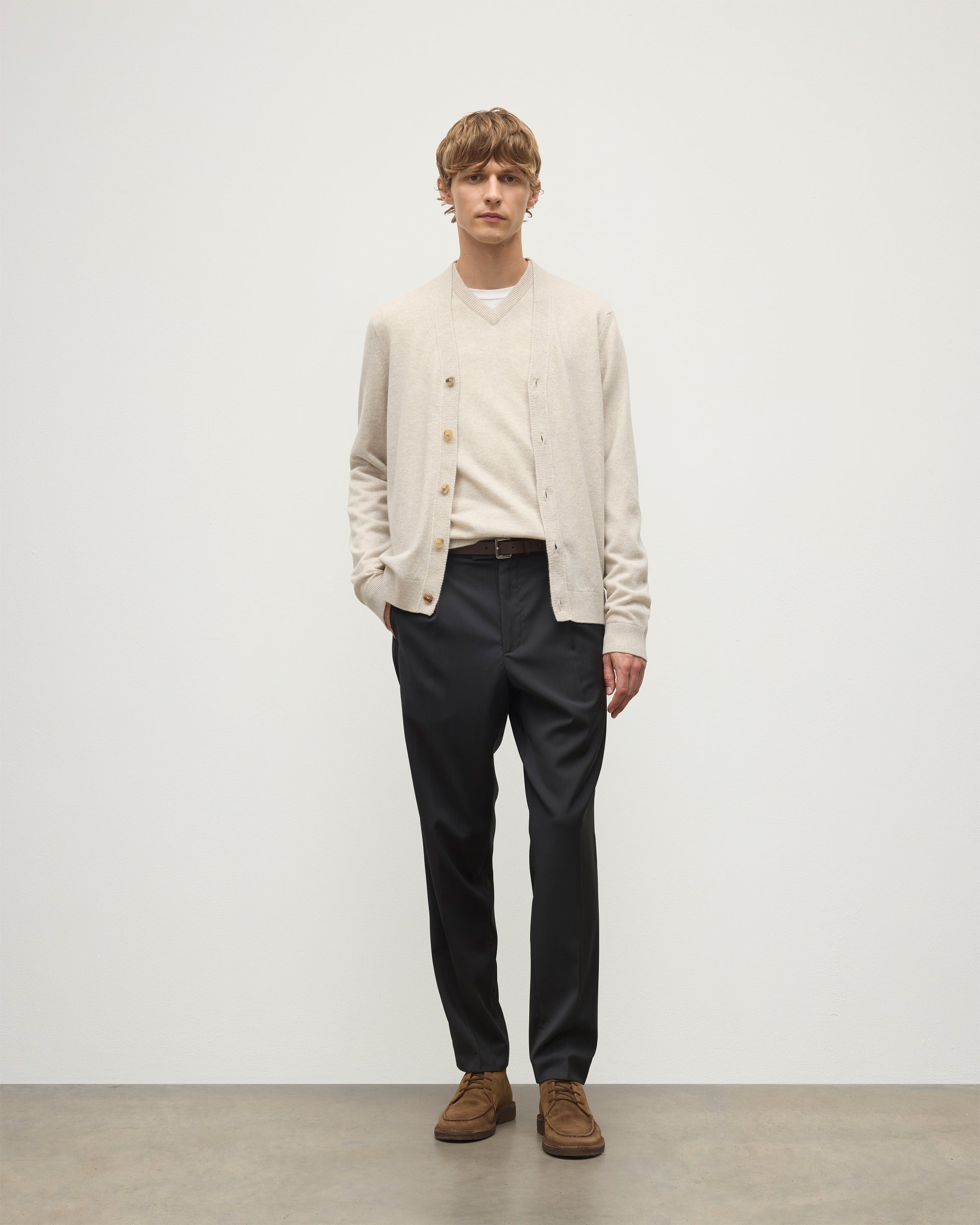 MODEL WEARS JOHNSTONS OF ELGIN MENS RORY VEE NECK CLASSIC CARDIGAN NATURAL 100% CASHMERE OVER A MATCHING V NECK SWEATER WITH GREY TROIUSERS KAP05576HA0402