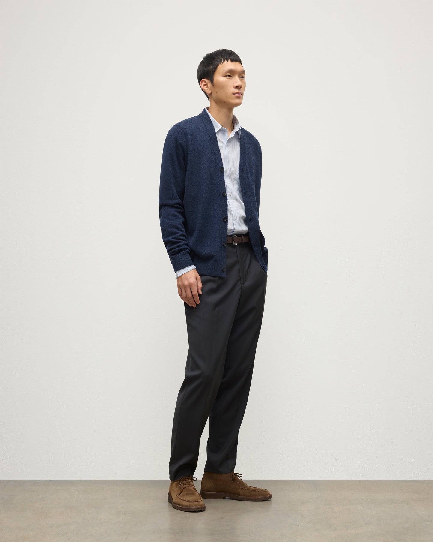 MODEL WEARS JOHNSTONS OF ELGIN MENS RORY VEE NECK CLASSIC CARDIGAN NAVY 100% CASHMERE OVER A LIGHT BLUE SHIRT WITH NAVY TROUSERS KAP05576HD7350