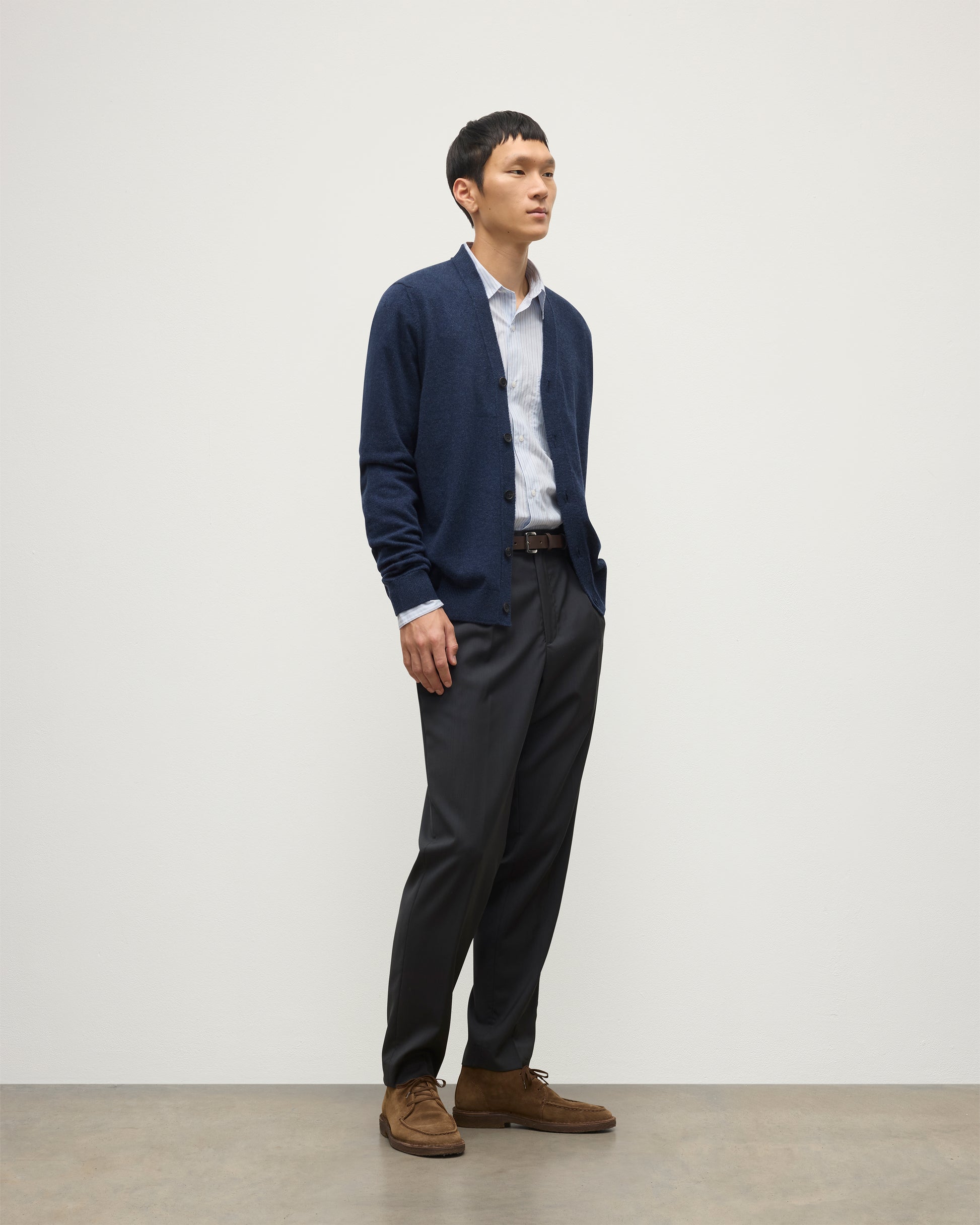 MODEL WEARS JOHNSTONS OF ELGIN MENS RORY VEE NECK CLASSIC CARDIGAN NAVY 100% CASHMERE OVER A LIGHT BLUE SHIRT WITH NAVY TROUSERS KAP05576HD7350