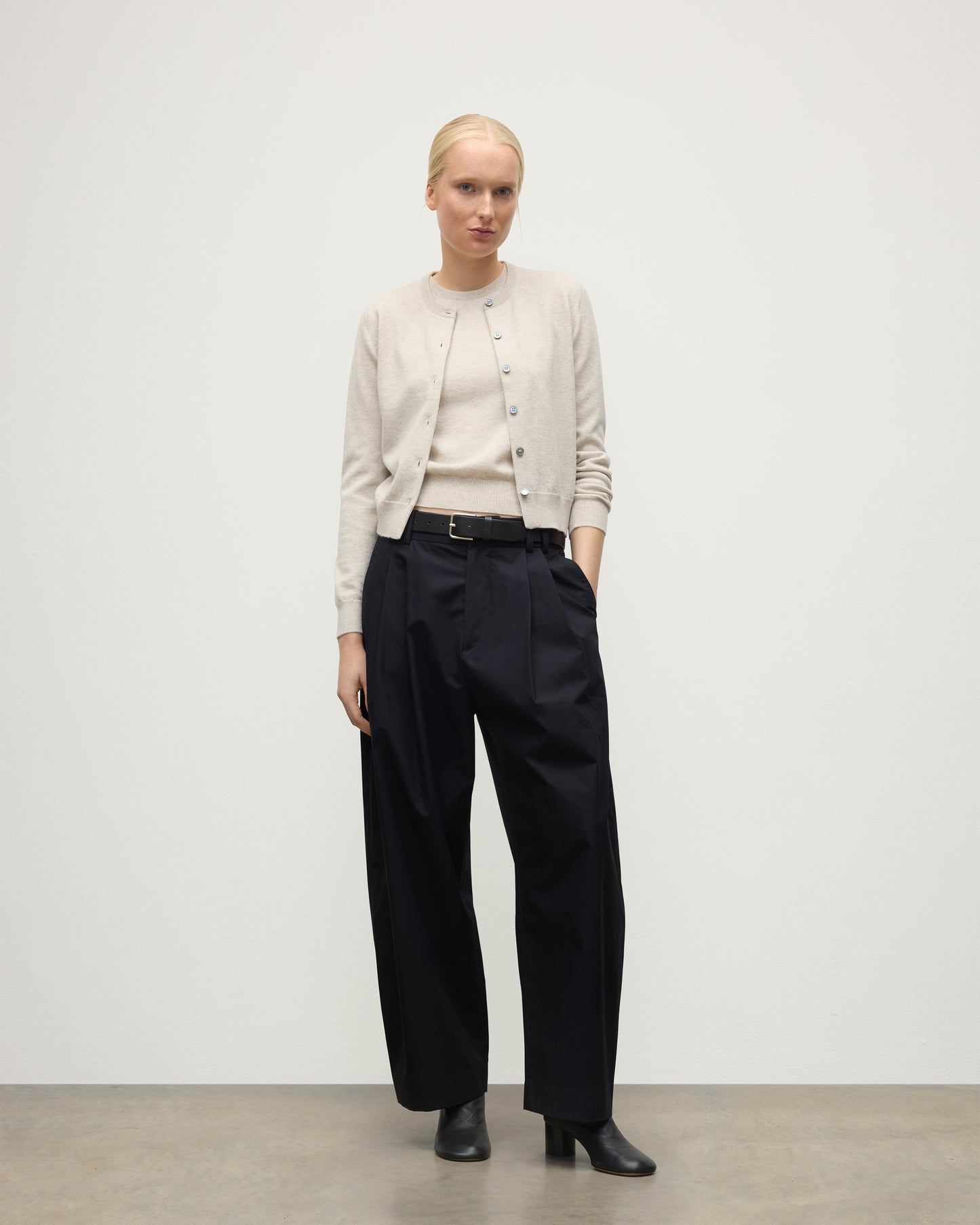 MODEL WEARING JOHNSTONS OF ELGIN WOMENS IRIS CLASSIC CREW CARDIGAN NATURAL 100% CASHMERE WITH NAVY TROUSERS AND BLACK BOOTS KAP05704HA0402