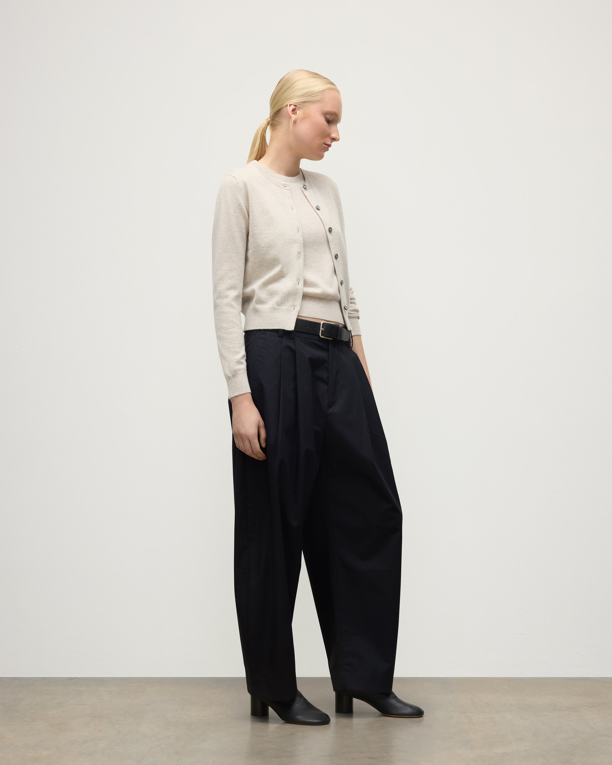 MODEL WEARING JOHNSTONS OF ELGIN WOMENS IRIS CLASSIC CREW CARDIGAN NATURAL 100% CASHMERE WITH NAVY TROUSERS AND BLACK BOOTS KAP05704HA0402