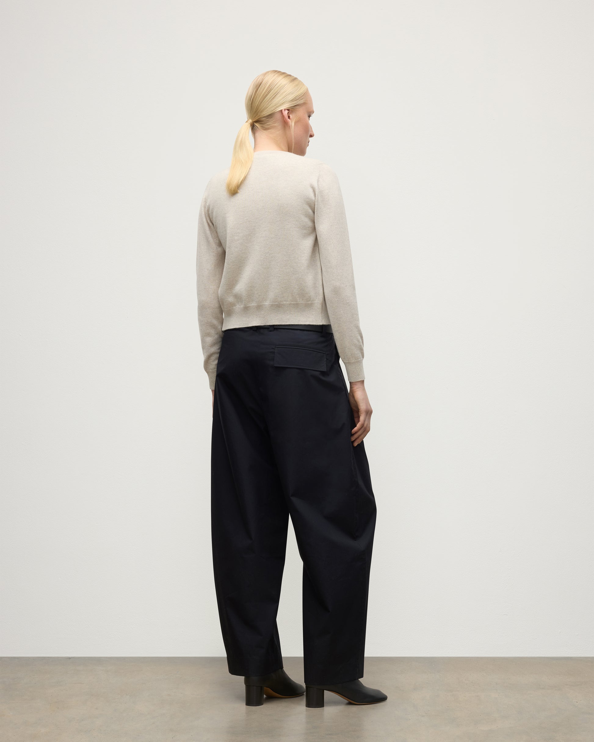 MODEL WEARING JOHNSTONS OF ELGIN WOMENS IRIS CLASSIC CREW CARDIGAN NATURAL 100% CASHMERE WITH NAVY TROUSERS AND BLACK BOOTS KAP05704HA0402