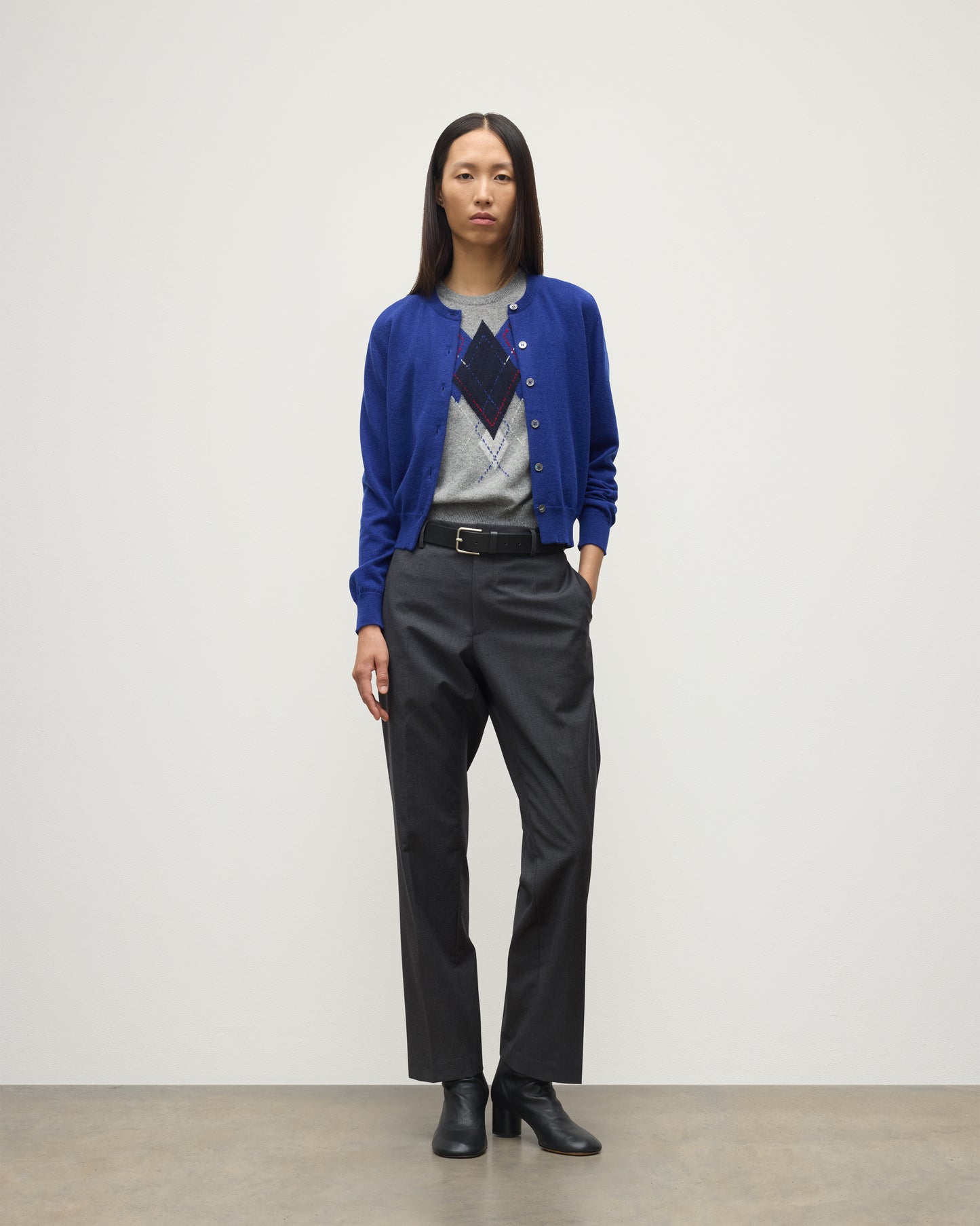 MODEL WEARING JOHNSTONS OF ELGIN WOMENS IRIS CLASSIC CREW CARDIGAN BLUE 100% CASHMERE OVER LE JABOT CASHMERE TANK WITH GREY TROUSERS AND BLACK BOOTS KAP05704SD5326