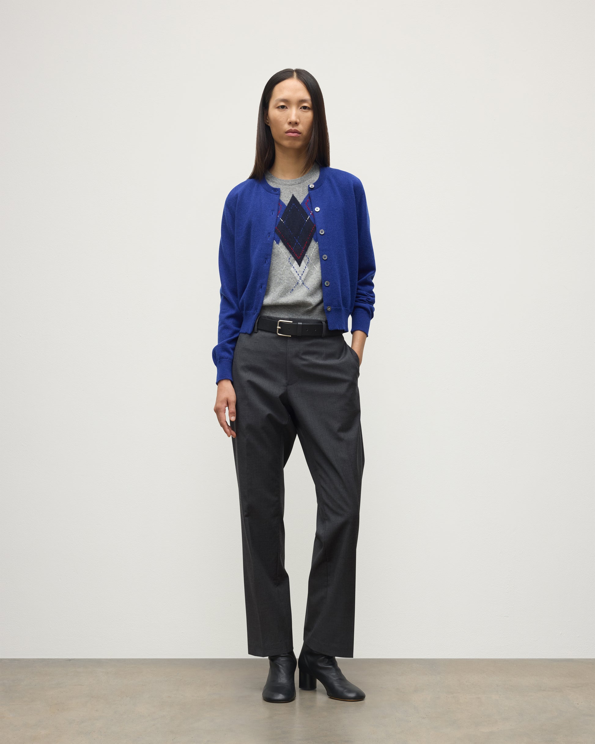 MODEL WEARING JOHNSTONS OF ELGIN WOMENS IRIS CLASSIC CREW CARDIGAN BLUE 100% CASHMERE OVER LE JABOT CASHMERE TANK WITH GREY TROUSERS AND BLACK BOOTS KAP05704SD5326
