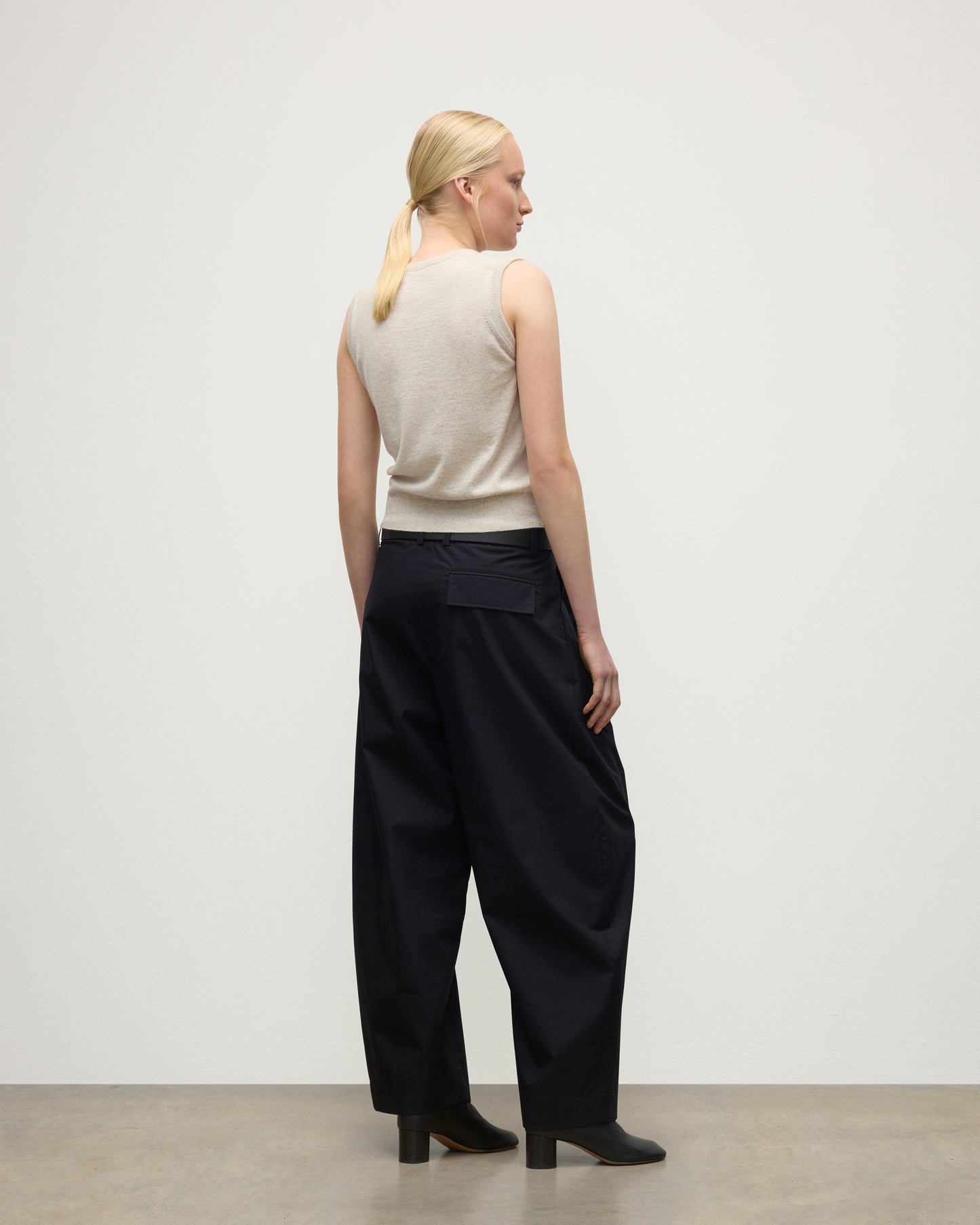 MODEL WEARS JOHNSTONS OF ELGIN WOMENS IRIS CLASSIC SLEEVELESS CREW NATURAL 100% CASHMERE WITH NAVY TROUSERS AND BLACK BOOTS  KAP05705HA0402