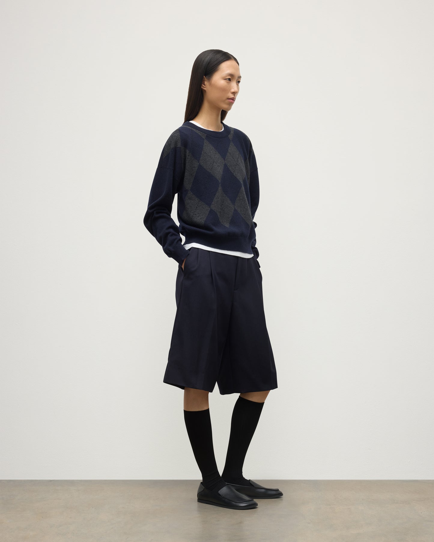 MODEL WEARS JOHNSTONS OF ELGIN WOMENS CLAN SLOUCH CREW NAVY 100% CASHMERE OVER A WHITE TEE, WITH NAVY LONG SHORTS, CASHMERE SOCKS AND LOAFERS KAP05732JU1606