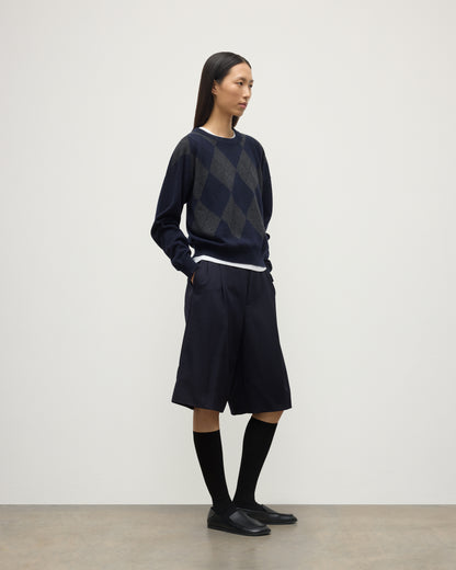 MODEL WEARS JOHNSTONS OF ELGIN WOMENS CLAN SLOUCH CREW NAVY 100% CASHMERE OVER A WHITE TEE, WITH NAVY LONG SHORTS, CASHMERE SOCKS AND LOAFERS KAP05732JU1606