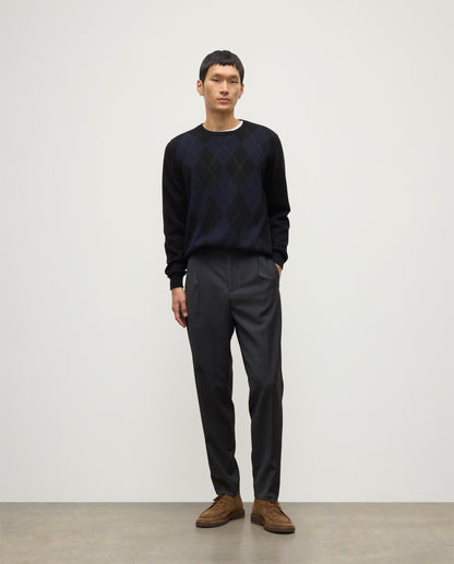 MODEL WEARING JOHNSTONS OF ELGIN MENS BLACK ARGYLL CREW SWEATER 100% CASHMERE OVER A WHITE T-SHIRT WITH NAVY TROUSERS KAP05747JU1599