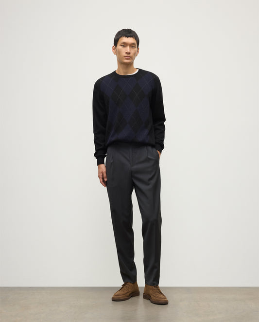MODEL WEARING JOHNSTONS OF ELGIN MENS BLACK ARGYLL CREW SWEATER 100% CASHMERE OVER A WHITE T-SHIRT WITH NAVY TROUSERS KAP05747JU1599