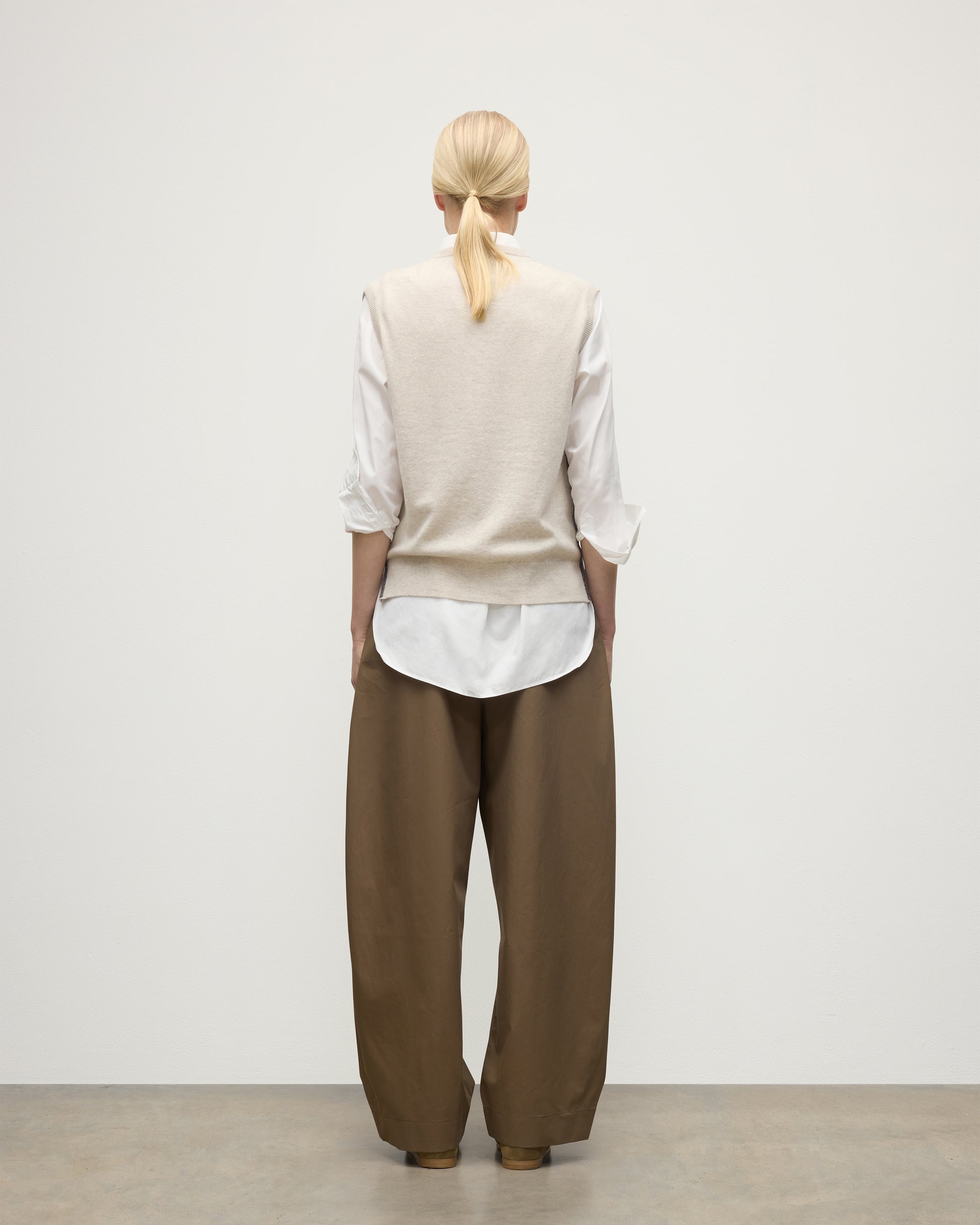 MODEL WEARS JOHNSTONS OF ELGIN WOMENS TILDA SLEEVELESS VEE NATURAL 100% CASHMERE OVER A WHITE SHIRT, WITH BROWN TROUSERS KAP05767Q25969