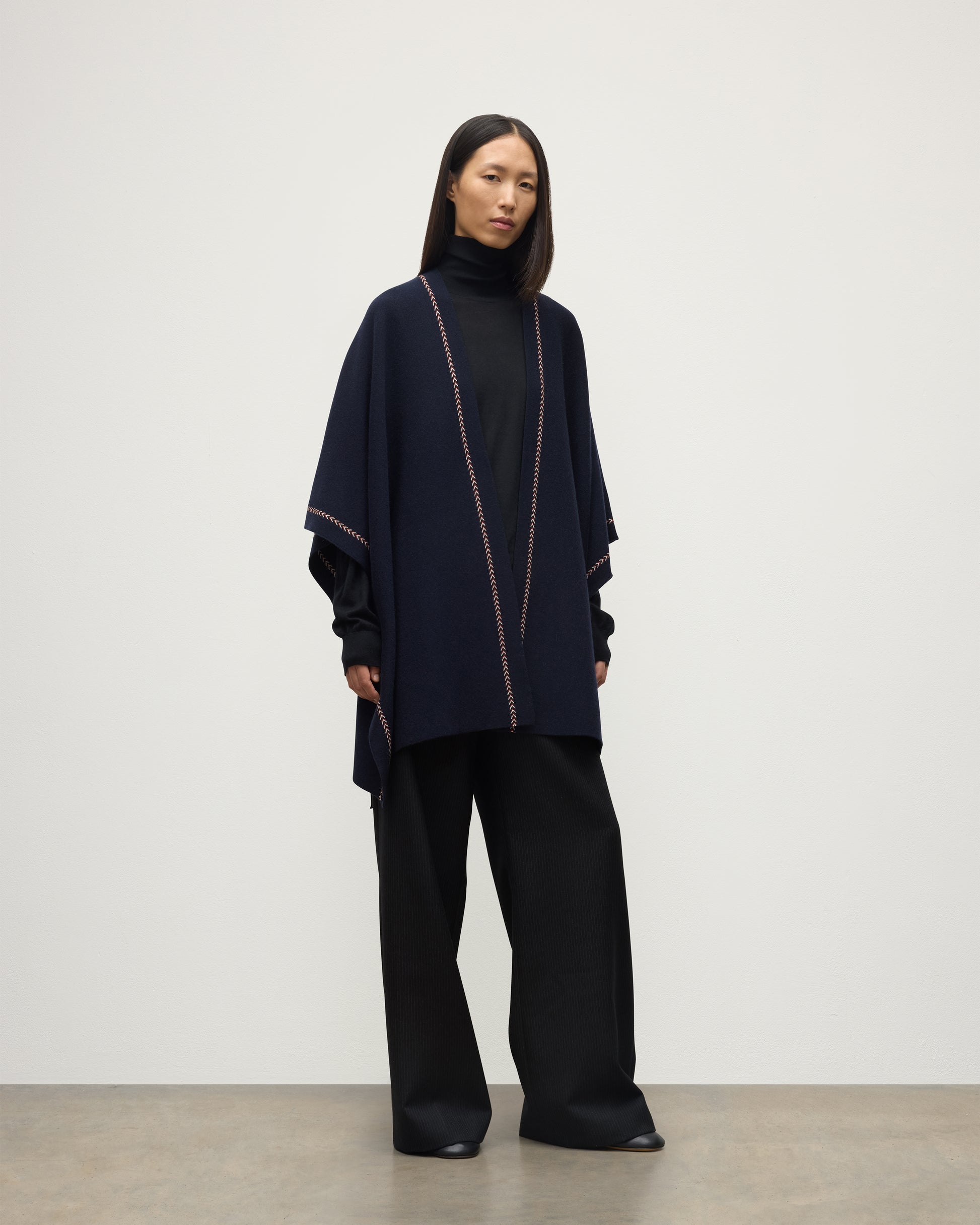 MODEL WEARS JOHNSTONS OF ELGIN WOMENS HAWK PONCHO NAVY 100% CASHMERE OVER NAVY ROLL NECK SWEATER AND NAVY TROUSERS KAU05769Q25973O/S